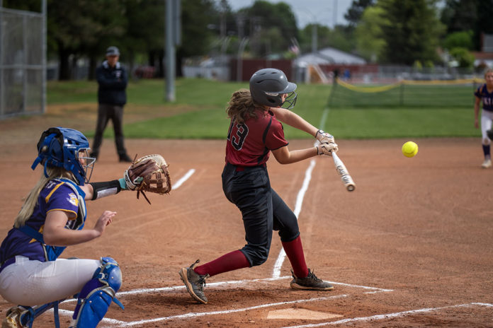 Girl hitting softball with catcher behind her